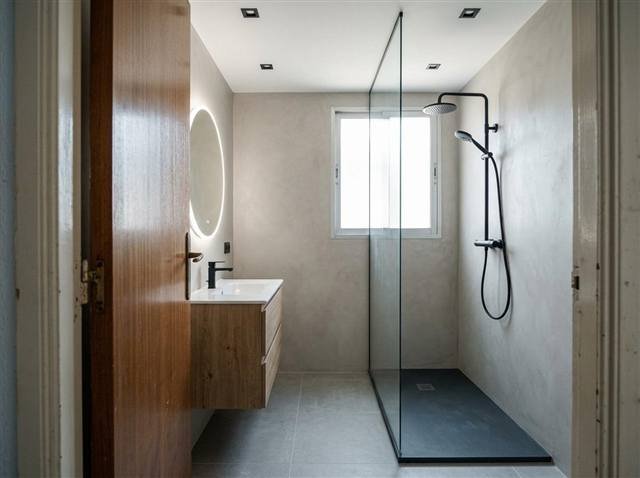 Después: ducha a ras de suelo con mampara fija, microcemento y mueble de roble suspendido